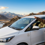 Best taxi service in Leh Ladakh 2026 - professional Ladakhi driver with white Toyota Innova SUV at viewpoint overlooking Indus River valley