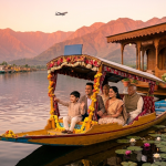 Kashmir packages from Hyderabad for family 2026 - happy multi-generational family on Shikara at Dal Lake golden hour with houseboat and airplane silhouette