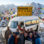 Ladakh group tour from Mumbai 2026 - happy group of travelers from Mumbai at Khardung La pass 18380 feet with tempo traveller