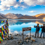 Ladakh tourism 2026 - Pangong Tso lake with snow-capped Himalayan mountains and travelers capturing the moment