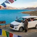 Leh to Pangong Lake taxi fare 2026 - white SUV taxi at Pangong Tso with turquoise-blue lake and snow-capped Himalayan mountains