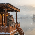 Kashmir winter honeymoon with houseboat showing couple on Dal Lake houseboat deck with snowfall and mountain views